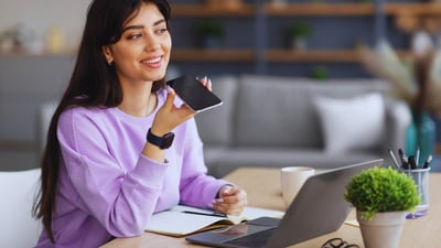woman talking into cellular phone in front of a laptop