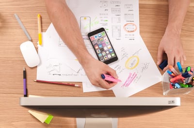 masculine arms in front of computer monitor with cell phone organizing design with colored markers