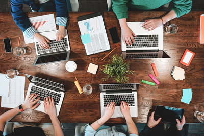 Group of coworkers working around a conference table using laptops and notebooks.