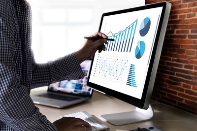 Man standing in front of a desktop computer with graphical information displayed.