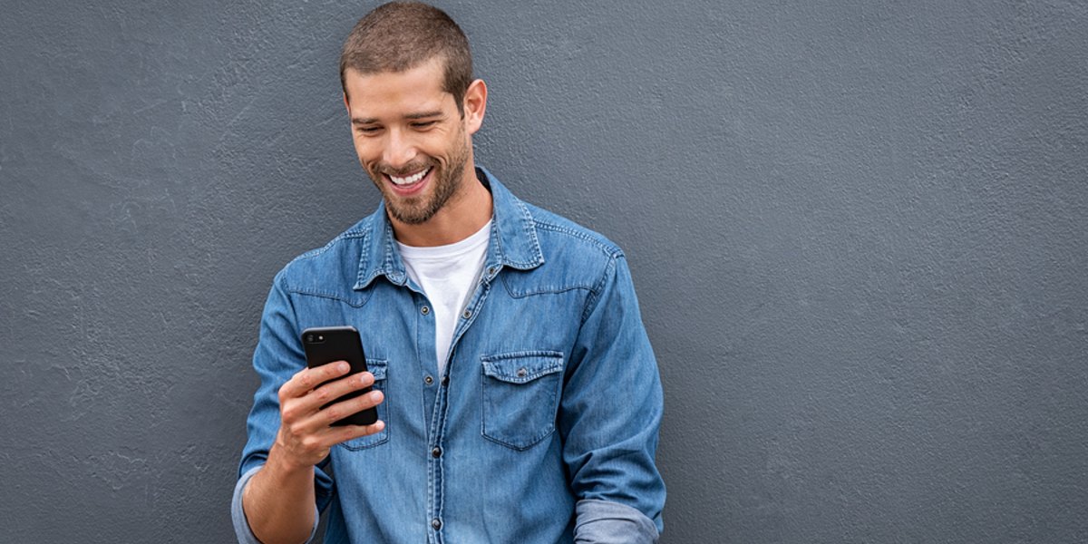 Smiling man leaning against a wall looking at his phone.