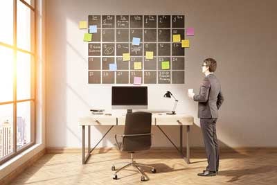 man standing looking at oversized calendar on the wall above a desk and computer