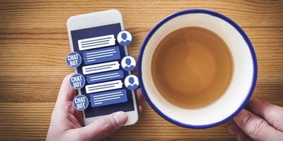 blue and white cell phone with chatbot conversation next to blue and white coffee cup on wooden table