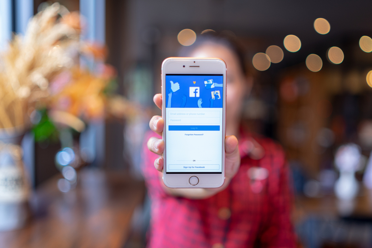 Person holding up a phone with the Facebook app displayed.