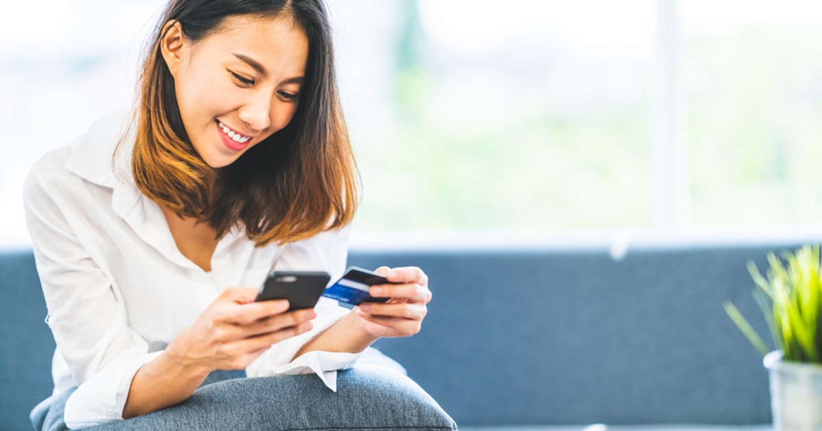 Smiling woman holding a credit card in one hand and her phone in the other.