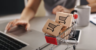 Miniature shopping cart with tiny brown boxes.