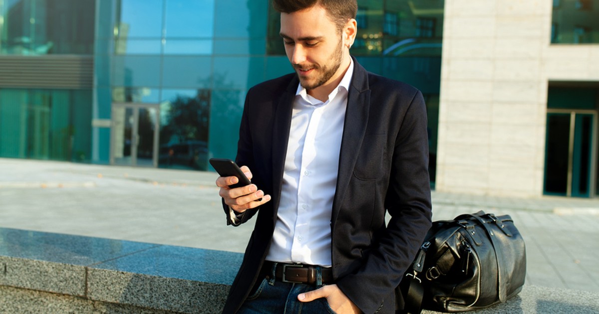 Man leaning against a wall looking at his phone.