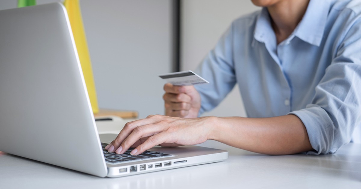 Man typing on a laptop while holding a credit card.
