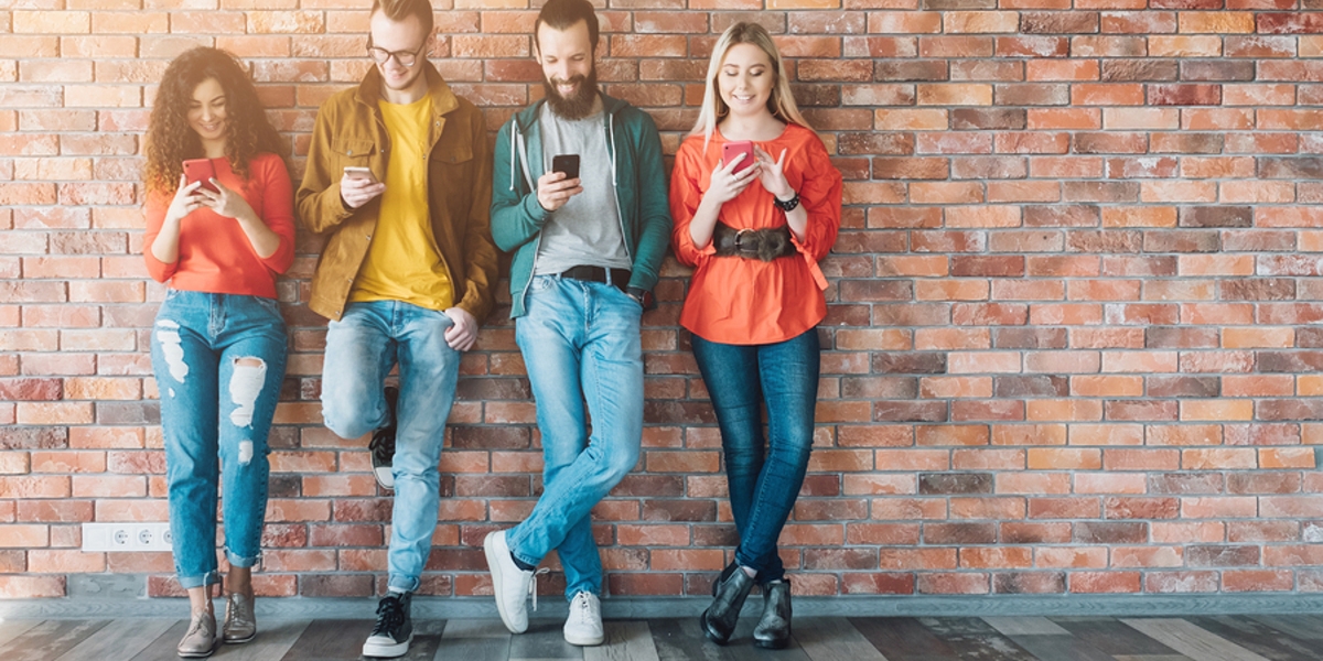 Group of young adults standing against a well looking at their phones.