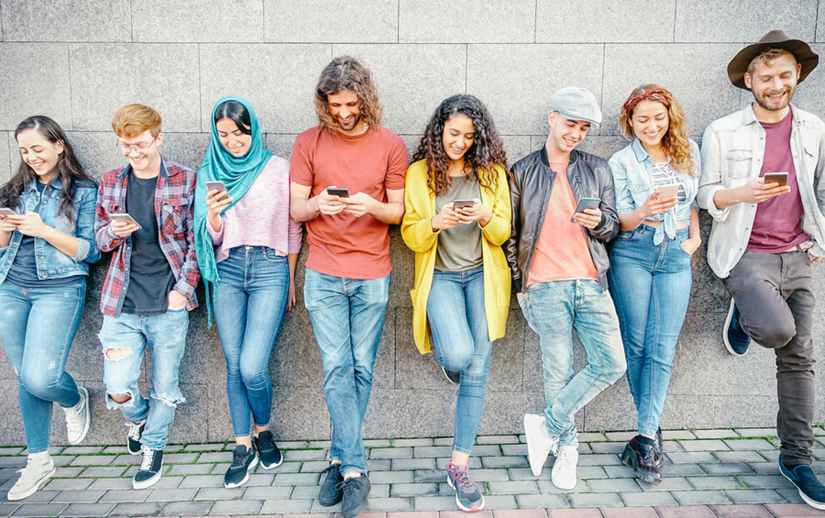 Group of people leaning against a stone wall looking at their phones and smiling.